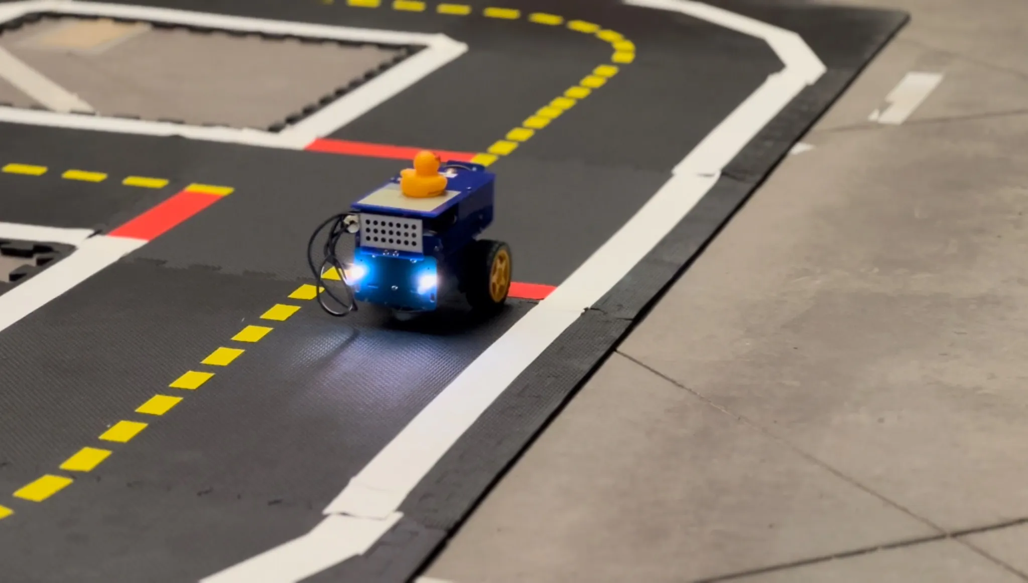 A small autonomous driving robot navigating a marked indoor road course